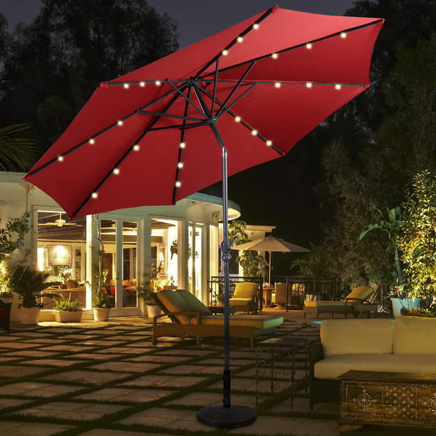 Red Sunergy patio umbrella with solar-powered lights illuminating an outdoor seating area at dusk